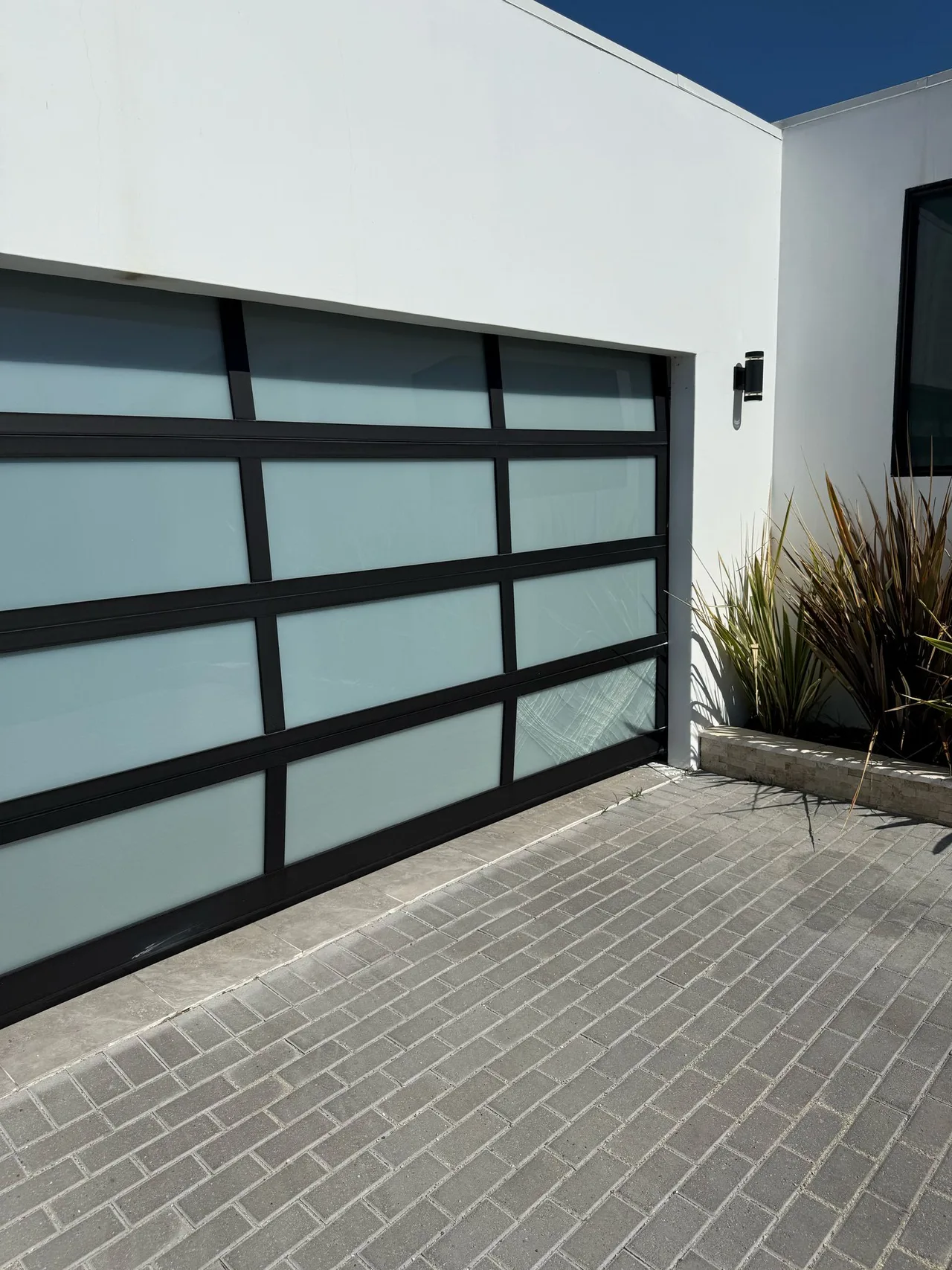 Glass-paneled garage door in a black frame beside a white wall