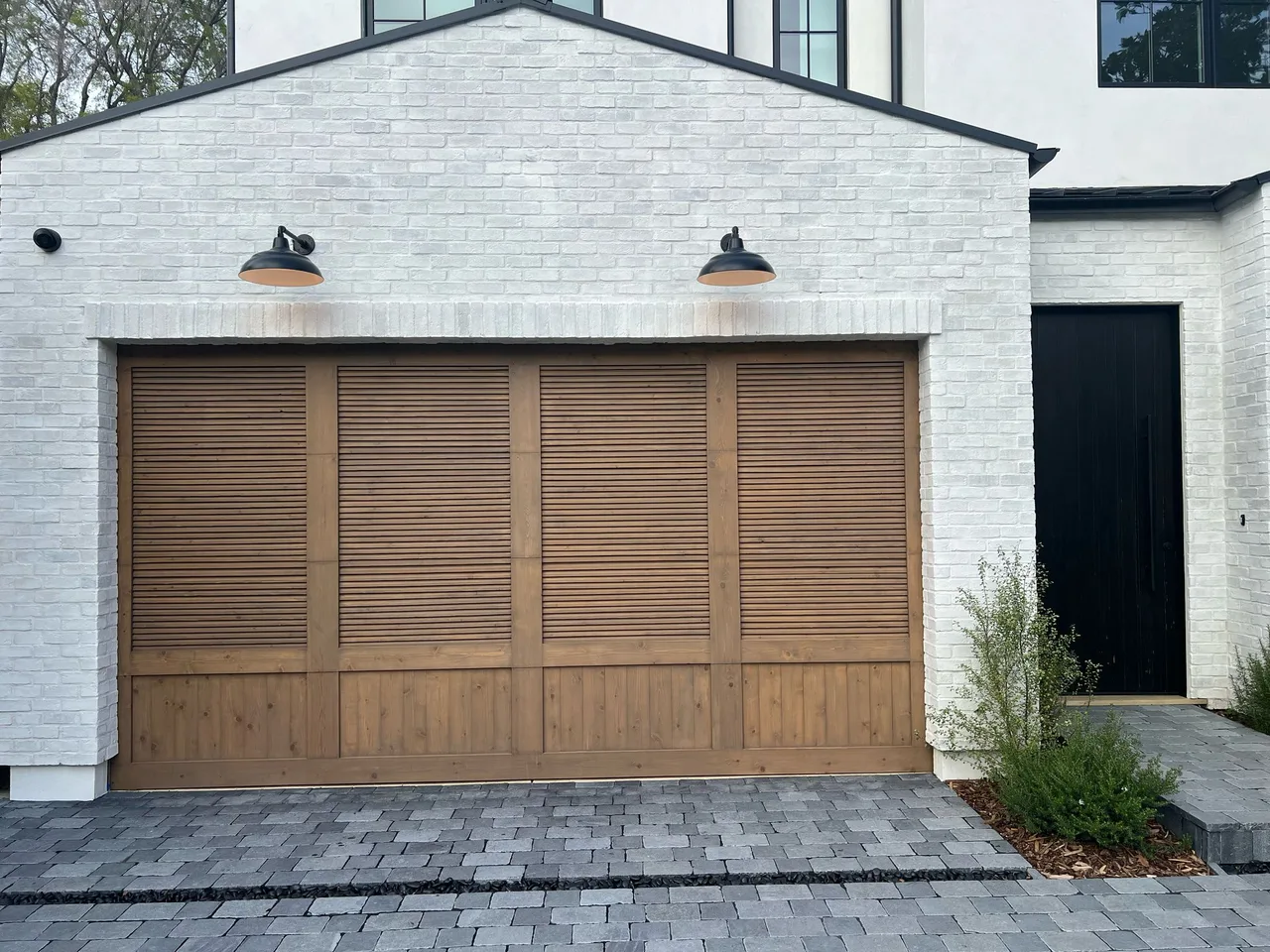 Wood-toned garage door with louvered panels on a white-brick facade